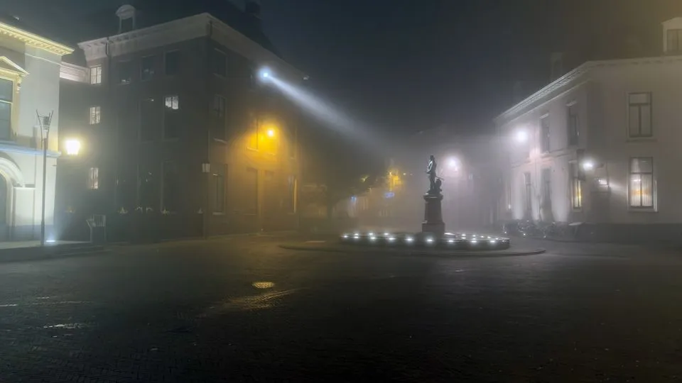 Een plein in de Leeuwarder binnenstad bij nacht in dichte mist, met een verlicht standbeeld en lantaarns