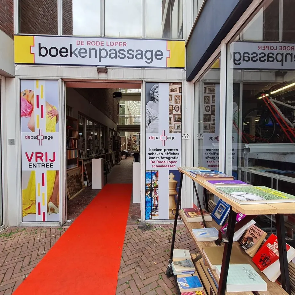 De ingang van Boekenpassage De Rode Loper aan de Sint Jacobsstraat, met het gele uithangbord en de rode loper op de klinkers