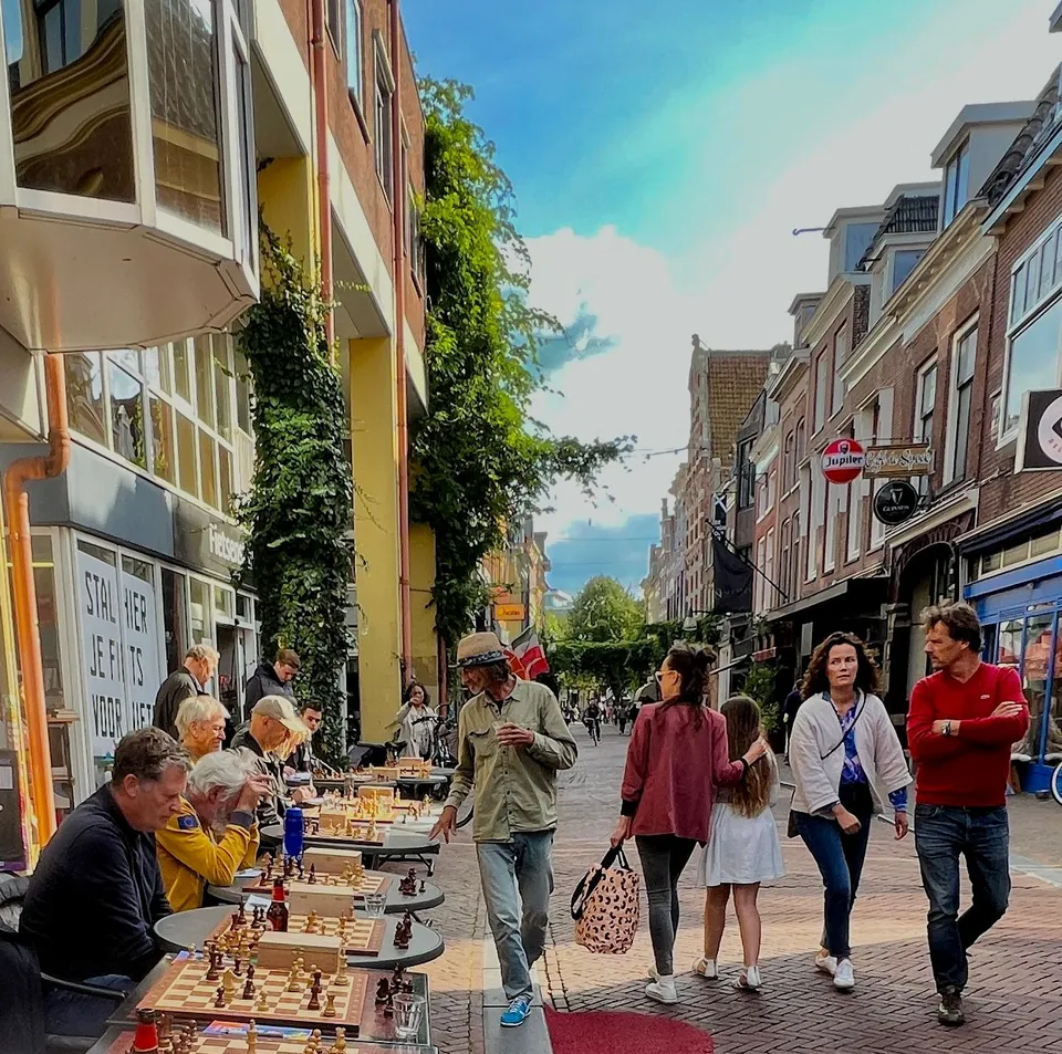 Rijen schaaktafels op straat voor de passage, met spelers en voorbijgangers in de Sint Jacobsstraat