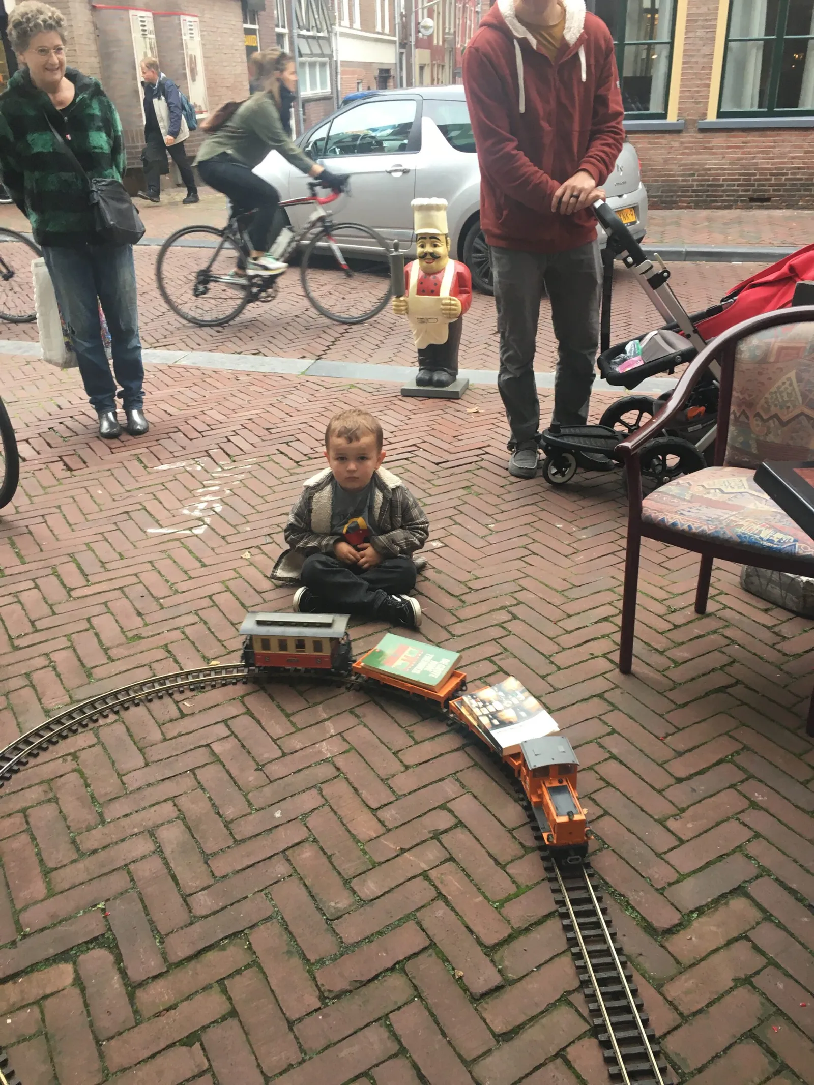 Een kind kijkt naar een speelgoedtrein die op rails uit de passage de straat op rijdt